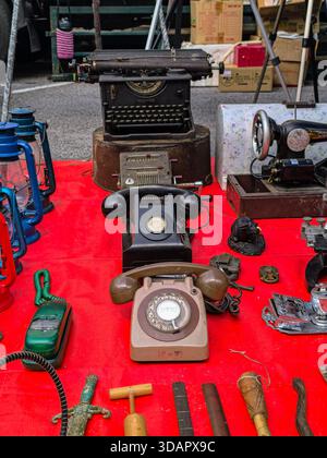 IPOH, MALAYSIA – NOVEMBER 09, 2025: Vintage telephones, lanterns, and an antique typewriter are displayed on a red cloth at a market stall. Stock Photo