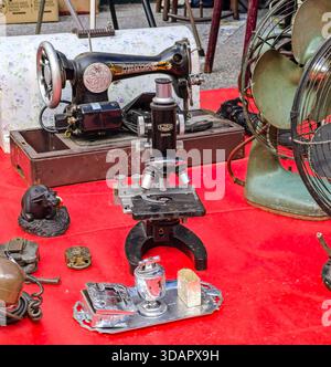 IPOH, MALAYSIA – NOVEMBER 09, 2025: An antique microscope and vintage sewing machine are displayed on a red cloth with other small items. Stock Photo
