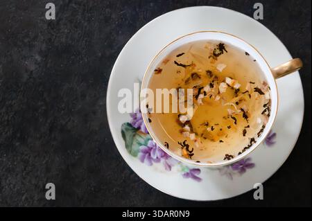 Top view of tea in a teacup, on a saucer with purple flowers, dark gray background Stock Photo