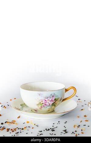 Empty teacup on saucer, tea leaves in foreground, white background, copy space above Stock Photo