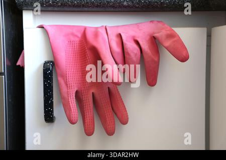 Close up of a pair of multipurpose rubber kitchen gloves hanging over a kitchen door cabinet door after being used. Stock Photo