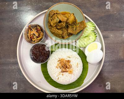A beautifully plated Nasi Lemak featuring fragrant rice on banana leaf, beef rendang, sambal, egg, cucumber, anchovies, and peanuts—an iconic Malaysia Stock Photo