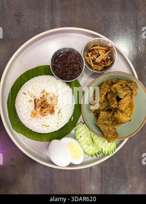 A beautifully plated Nasi Lemak featuring fragrant rice on banana leaf, beef rendang, sambal, egg, cucumber, anchovies, and peanuts—an iconic Malaysia Stock Photo