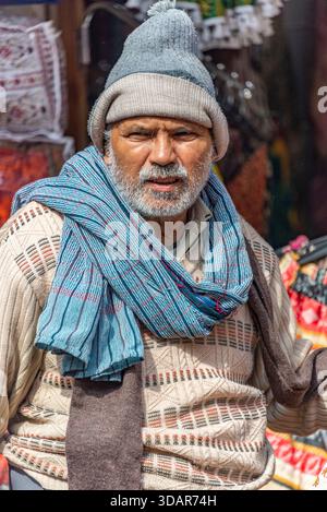 Elderly Man in Layered Winter Clothing Standing in Vibrant Indian Street Market. Pushkar, Rajasthan, India, 28 Jan 2024 Stock Photo