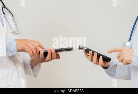 Two hospital doctors, a woman and a man, taking a break and watching or sharing something on their phone over white background. Stock Photo