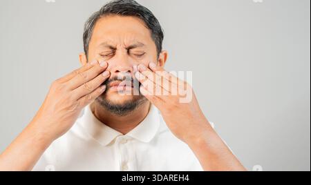 Asian bearded man with eye pain and suffering from eyestrain standing on white background, Diabetic Retinopathy, Pinguecula or Pterygium concept Stock Photo