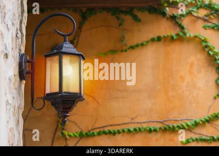 Vintage hexagon metal lamp mockup hanging on a brick wall with blurred image of an old orange wall with ivy background. Copy space. Stock Photo