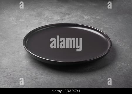 empty round black ceramic plate on dark grey textured concrete or slate surface, elegant monochrome industrial background for fine dining presentation Stock Photo