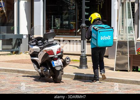 Riga, Latvia - May 29, 2021: A delivery worker approaches a shop while leaving a scooter parked nearby in a city street. Stock Photo