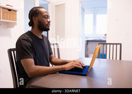 Digital Productivity in a Clean Workspace. Black man working on a laptop in complementary colors. Stock Photo