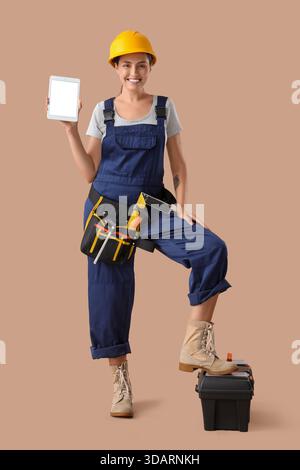 Female builder with blank tablet computer and tools on beige background Stock Photo