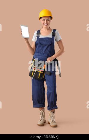 Female builder with blank tablet computer on beige background Stock Photo