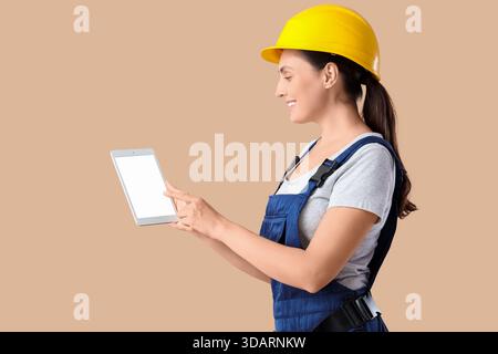 Female builder with blank tablet computer on beige background Stock Photo