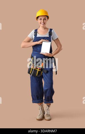 Female builder with blank tablet computer on beige background Stock Photo