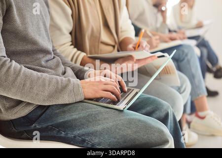 Group of students sitting in line working on laptops, writing in notes and waiting for class Stock Photo