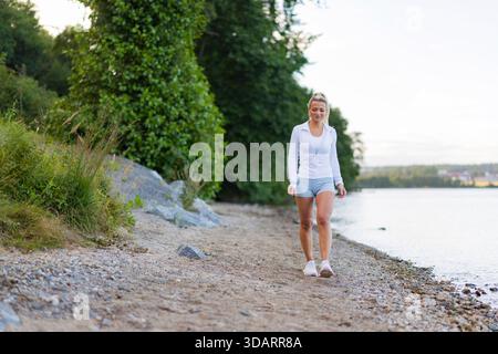 Woman walking on a scenic trail by the lake in outdoor activewear Stock Photo