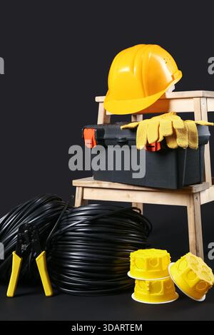 Stepladder with electrician tools, rolled cables and hardhat on black background Stock Photo