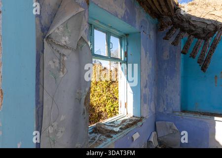 Sunlit abandoned room with peeling blue walls, broken window, and remnants of old wallpaper, evoking nostalgia and urban decay. Stock Photo