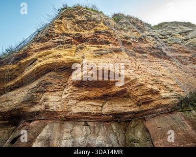Safety netting covering the textured sandstone cliff face below the castle in Knaresborough, North Yorkshire. Stock Photo