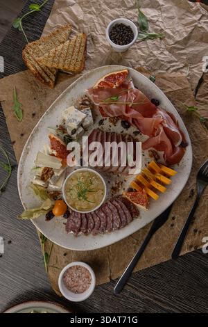Cold plate featuring assorted cheeses, cold cuts, and appetizers on rustic table Stock Photo