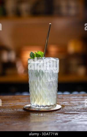 Refreshing lemon cocktail with ice decorated with mint leaf on a rustic wooden bar counter Stock Photo
