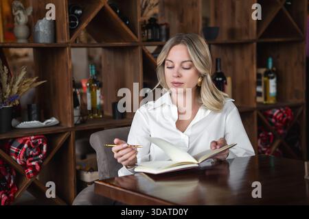 Woman writing in notebook at table in cafe. Focused, elegant. Stock Photo