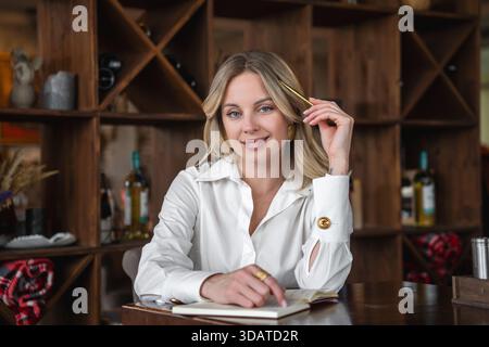 Woman writing in notebook at table in cafe. Focused, elegant. Stock Photo
