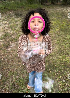 Child blows soap bubbles outdoors with a pink bubble wand. Stock Photo