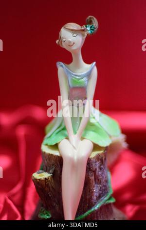 A whimsical figurine of a seated girl with a green dress on a red background. Stock Photo