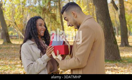 Hispanic couple woman giving present box to beloved man amazed surprised saying wow opening present birthday anniversary occasion married girl guy in Stock Photo