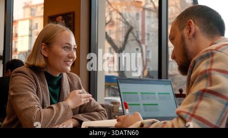 Two young people working together on a laptop in a cozy cafe setting Stock Photo