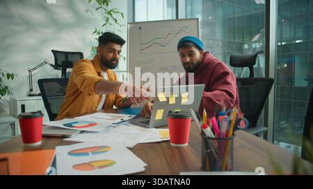 Two informal Indian businessmen Arabian business men co-workers males discussing project strategy in modern coworking office pointing at whiteboard Stock Photo