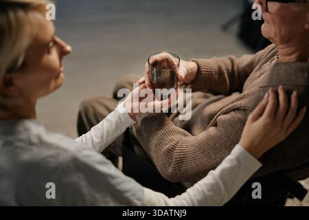 Caucasian Female Caregiver Assisting Senior Caucasian Man with Drinking Water Stock Photo
