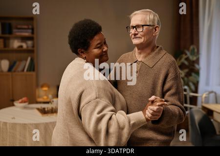 Senior Caucasian Man and Black Woman Smiling While Dancing Together Indoors Stock Photo