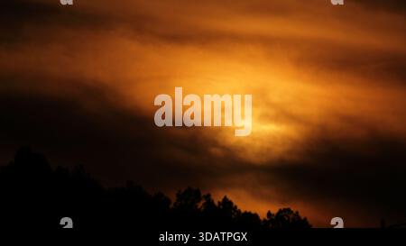 View of a fiery sunset paints the sky in shades of orange and black above the silhouetted trees in Margalla Hills National Park, Islamabad, Islamabad Stock Photo