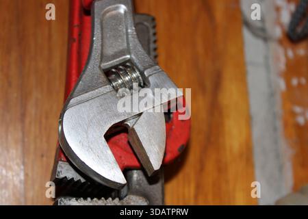 A metal wrench is shown alongside a pipe gripping tool on a wooden work surface. Tools are used for tightening and loosening during DIY home repair ta Stock Photo