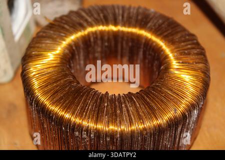 A copper wire coil rests on a wooden workbench with sunlight shining on it. The coil shows clear layers of copper wire. Tools and materials are visibl Stock Photo