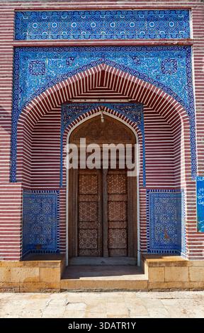 View of an ornately decorated doorway, featuring intricate blue tilework contrasting with red and white striped patterns, stands majestically, Thatta, Stock Photo