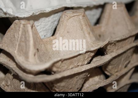 Several empty egg cartons are stacked neatly on a surface in a kitchen area of a local store. The light falls on the cartons, revealing their texture. Stock Photo