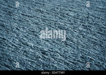 View of the rugged, icy terrain with deep blue shadows stretching across the uneven surface, showing an abstract, cold landscape, Bedretto, Ticino, Sw Stock Photo