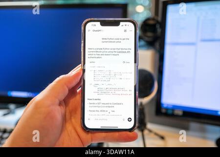 Illustrative image of a person's hand holding an iPhone and using the OpenAI ChatGPT app with GPT-5 model to write Python software code, with computer screens and office equipment in the background, Lafayette, California, August 7, 2025. (Photo by Smith Collection/Gado/Sipa USA) Stock Photo