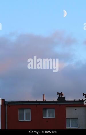 Crescent Moon and Clouds Over a Red Urban Building at Twilight Stock Photo