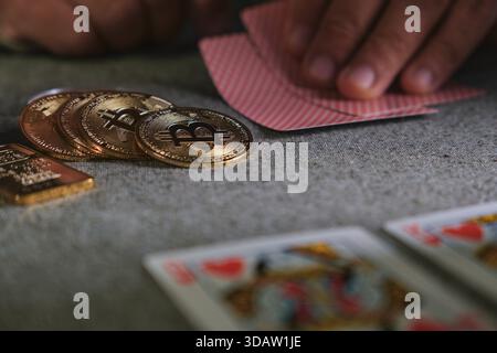 Hands holding playing cards next to crypto coins and a gold bar on a casino game Stock Photo