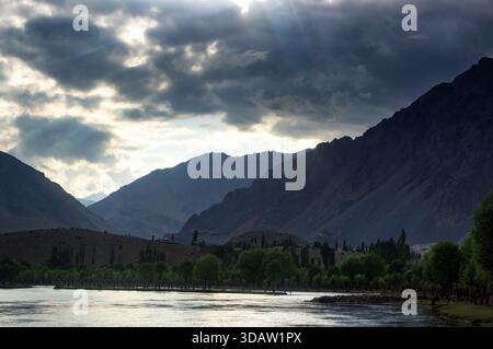 View of sunlight piercing through ominous clouds over a tranquil lake surrounded by majestic mountains, Gupis, Gilgit Baltistan, Pakistan. Stock Photo