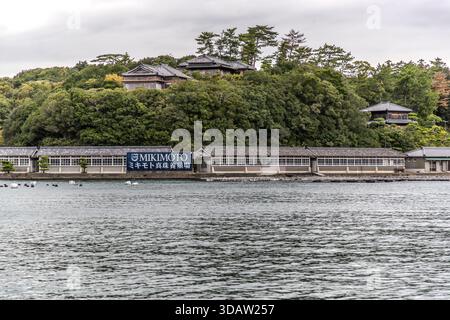 From the waters of Ago Bay, you can see the extensive facilities of the Mikimoto pearl farm. Mikimoto Pearl Farm with traditional buildings by the water in Shima, Mie, Japan Stock Photo