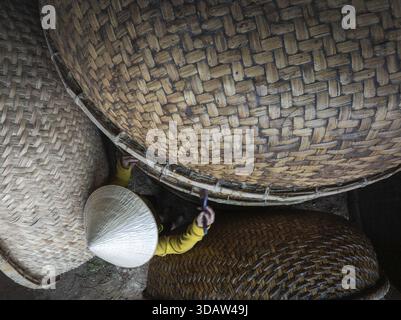 Aerial view of a woman in a conical hat surrounded by large woven baskets, creating a textural tapestry of light and shadow, Sông Cầu, Phú Yên, Vietna Stock Photo