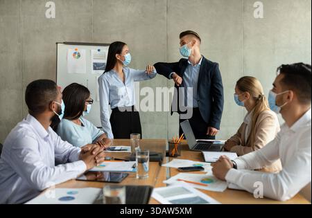 Coworkers Greeting Each Other With Elbow Bumps During Meeting in Modern Office Setting Stock Photo