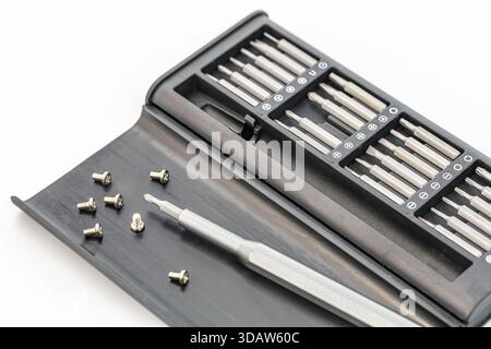 A screwdriver set is neatly organized in a black case, alongside a few small screws scattered on the lid. The set contains various types of heads for Stock Photo