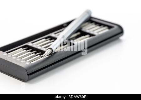A screwdriver with different bits in a box on a white surface. The screwdriver handle is gray, and the case is black. The screwdriver lies at an angle Stock Photo