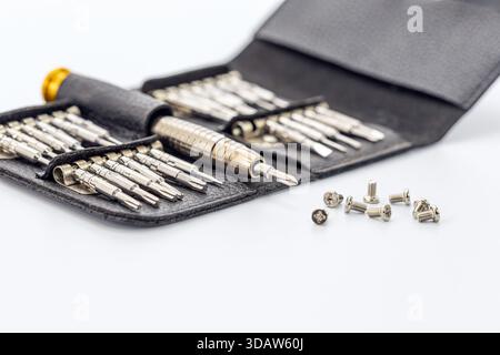 A set of precision screwdrivers with various bits in a black leather case with some screws on a white surface. Silver metal tools sit in pockets and o Stock Photo